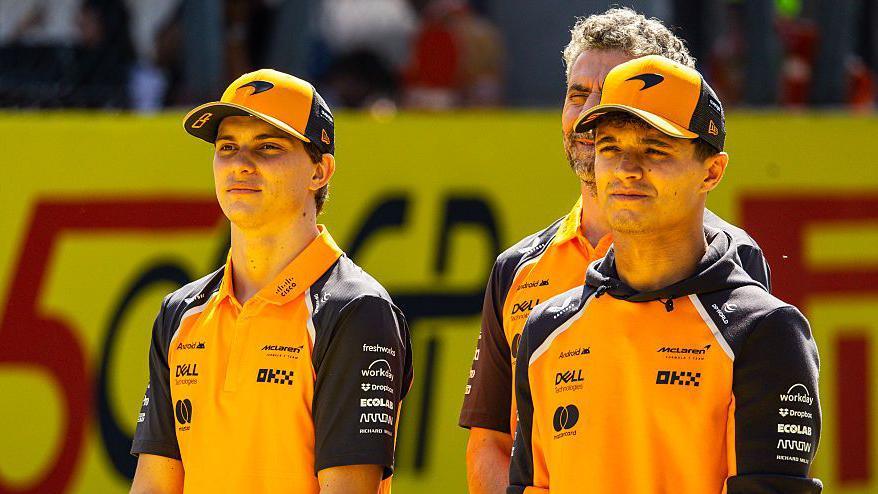 Oscar Piastri and Lando Norris standing in front of McLaren boss Andrea Stella 