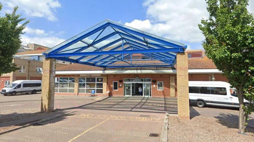 A hospital. The ground is light brown, there is a blue archway in the foreground. A green tree is on the right of the archway.