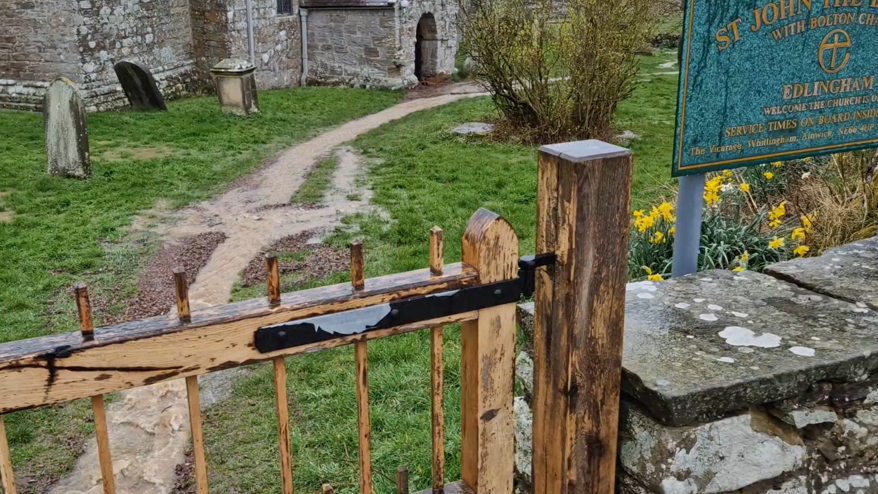 A rural church from the church gate with water running through the graveyard and into the church.