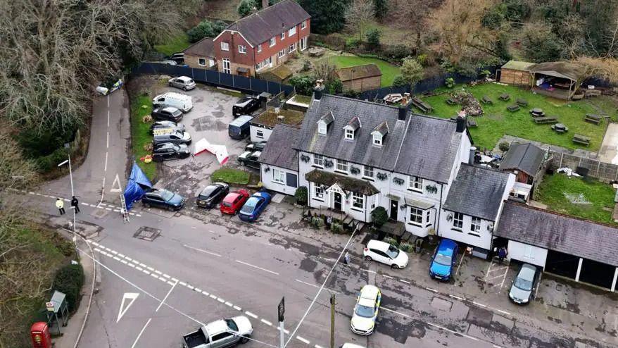 Aerial view of a large grey pub with a police cordon closing the road outside.