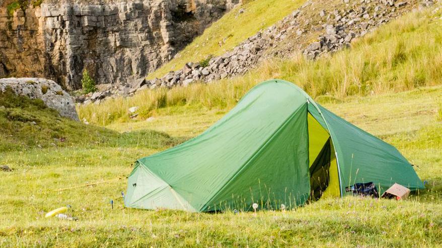 Picture taken on The Cambrian Way mountain and hill walking route from Cardiff in south Wales through the higher parts of central Wales to Conwy on the north Wales Coast. It shows a green tent in a green field with some rocks behind it