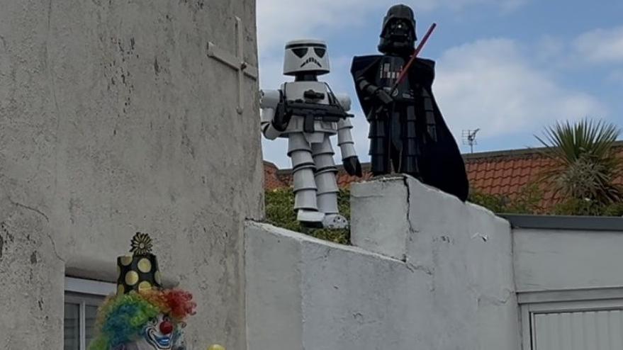 A white stormtrooper and a black Darth Vader stand on top of a white building.