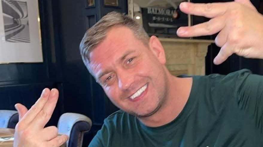 John George wearing a green t-shirt and smiling at the camera. He has short light hair.