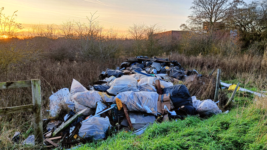 Rubbish bags full of cardboard boxes dumped in the countryside off Southend Road just outside of Chelmsford. The sun is setting in the sky.