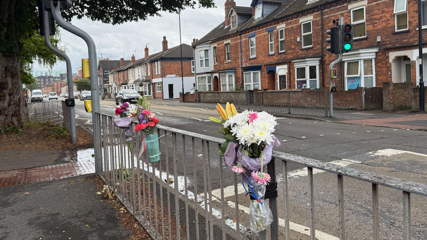 Three bunches of flowers tied to railings at a pedestrian crossing.