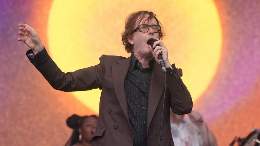 Jarvis Cocker, wearing glasses and a brown jacket with Pulp performing on the Pyramid Stage during the Glastonbury Festival at Worthy Farm in Somerset. 