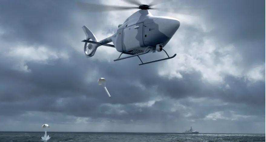 A computer generated image of a helicopter shaped autonomous aircraft dropping supplies into the sea. The craft is painted in combat style grey shades and the sky behind it is also dark and grey. 