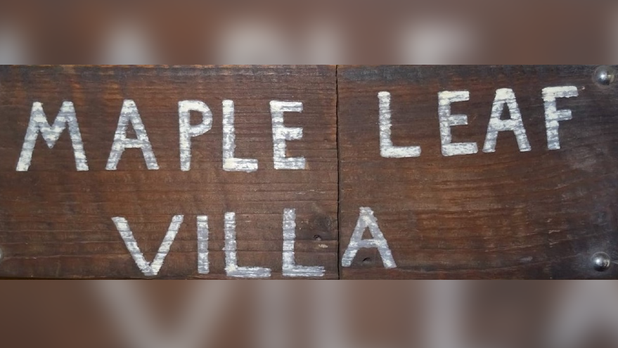 A dark plank of wood with a join in the middle and amateur white painted lettering in capitals reading Maple Leaf Villa