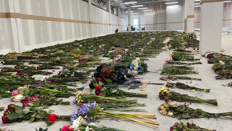 Rows of hundreds of bouquets of flowers laid out on the concrete floor of a warehouse.