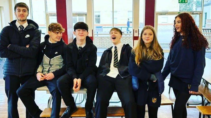 Osian Jones and his school friends sit on a bench in their school canteen in Penarth