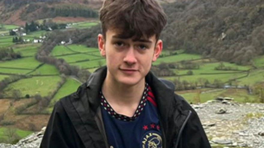 Lloyd Sutton on a hike. He is wearing a black jacket and dark blue t-shirt. He has brown hair.