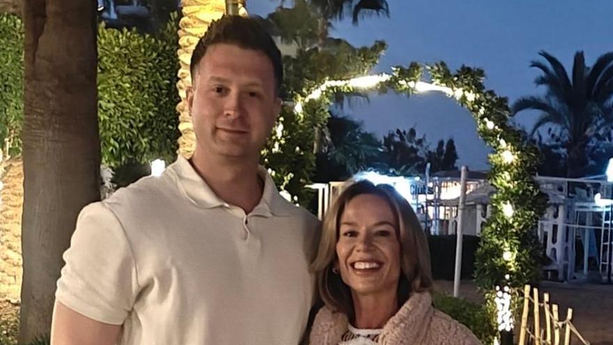 A photo of a couple standing together. A man with a white top and a woman with a fluffy jacket on. They are both smiling. 