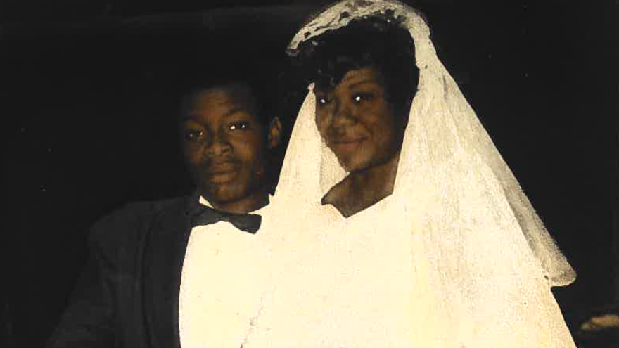 The photo shows Mervis and George on their wedding day. George is wearing black tie and Mervis is wearing a white dress and veil.