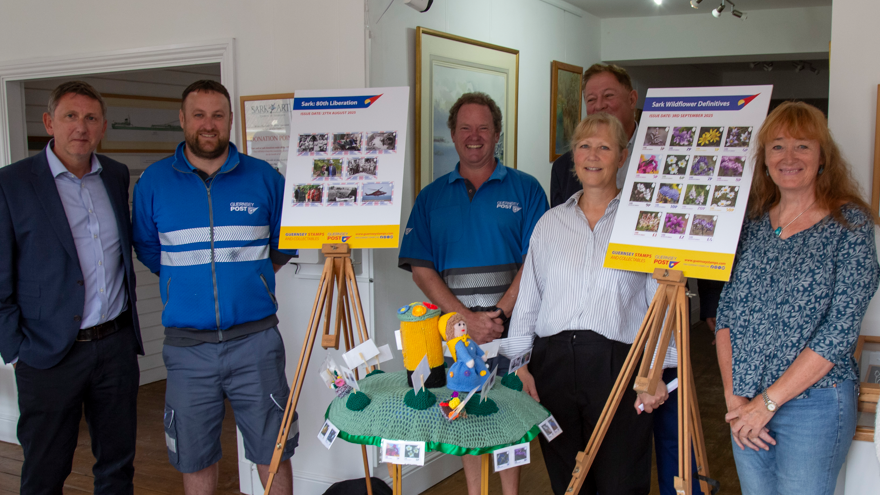 People stood around easels which are holding photos of stamps being issued in Sark.