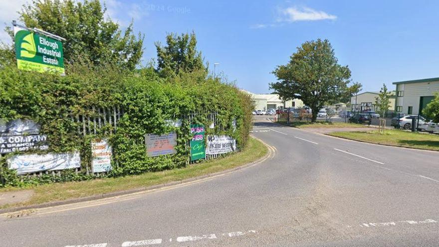 A general view of Benacre Road near Ellough and the entrance to the Ellough Industrial Estate. A car can be seen leaving the estate and approaching the junction. Industrial buildings can be seen in the distance. 