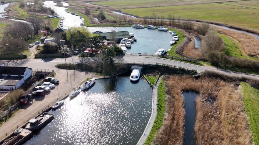 A bird's eye view of the bridge at Ludham, which has marshland on one side and buildings in the foreground.