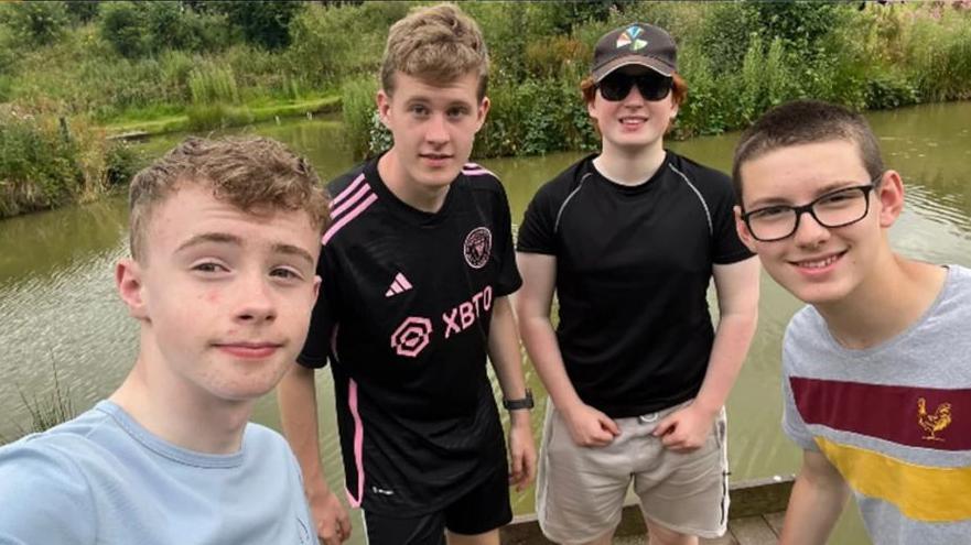 Four teenage boys posing for a photo in front of a river