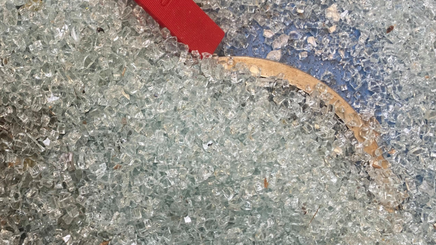 Smashed glass all over the ground and a wooden frame and red sticky velcro material on the glass