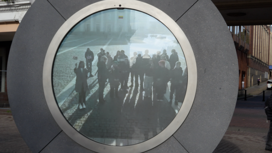 A circle portal was stood in the middle of the image. It was made out of silver material and had a screen in the middle which showed people standing in it.
