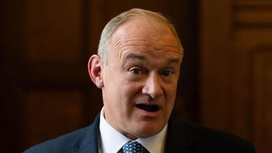 Ed Davey with mouth open, against a dark background