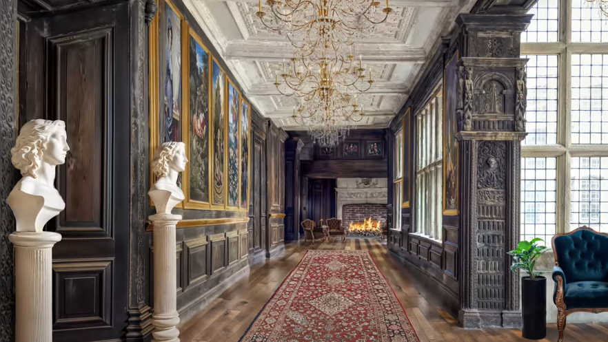 A computer generated image of how the Long Gallery at Hopwood Hall could look after renovation. There are two Roman-style busts on plinths and a long rug running down the corridor, with golden chandeliers hanging from the ceiling. 