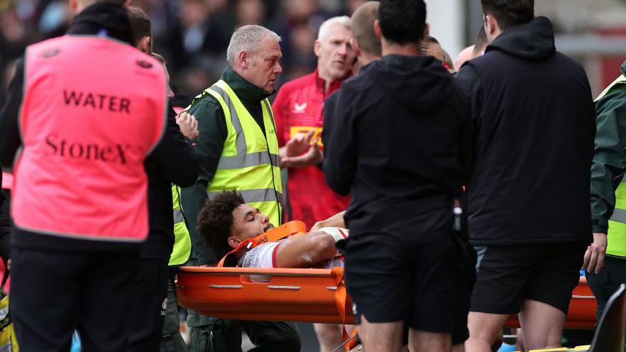 Andy Onyeama-Christie of Saracens is carried off after being injured during the Gallagher Premiership Rugby match between Harlequins and Saracens at The Stoop on October 13, 2024 in London, England.