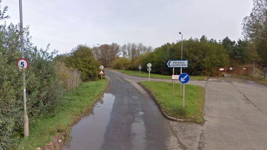 Road leading to Daneshill Landfill, showing a small road sign and alongside hedges and small trees