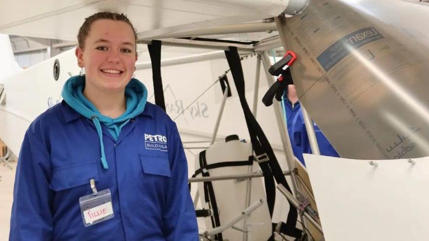 Tillie Baker stands in front of the plane in a workshop