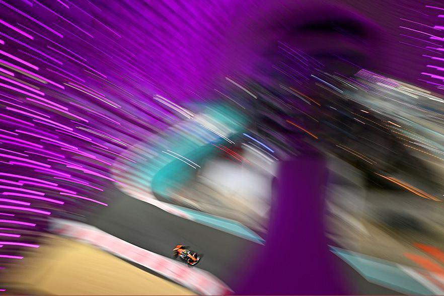 A Formula 1 car driven by Lando Norris speeds along the track, with purple lights creating a dramatic motion blur effect