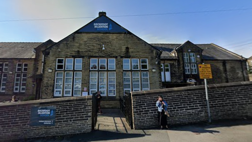 A stone school building with large glass windows and a wall in front of the building 