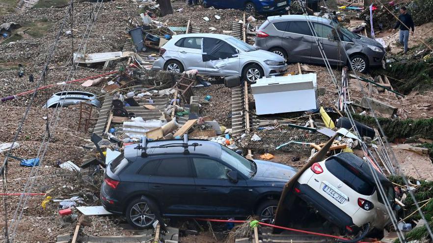 People walk among wrecked cars spread along a railway track after the floods in Spain. 