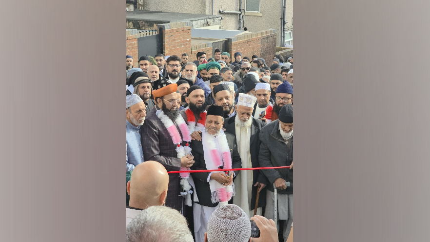 A crowd of men smiling, waiting to cut a red ribbon 