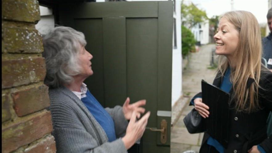 Sian Berry talks to a resident with the door of her home ajar