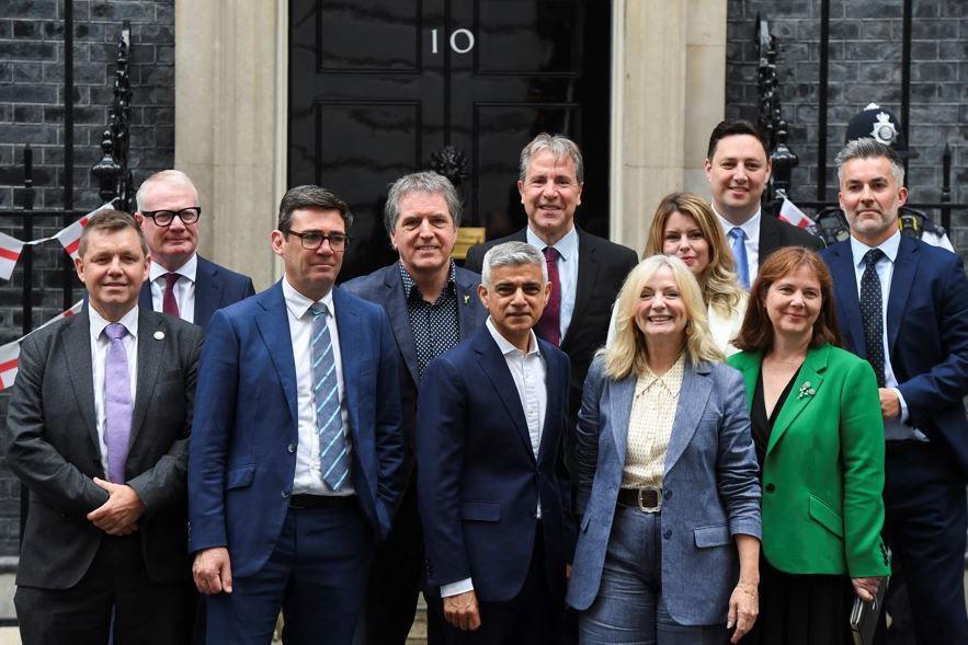 Eleven people wearing suits and blazers huddled up outside 10 Downing Street, including Nik Johnson standing far left. London mayor Sadiq Khan is standing centrally.