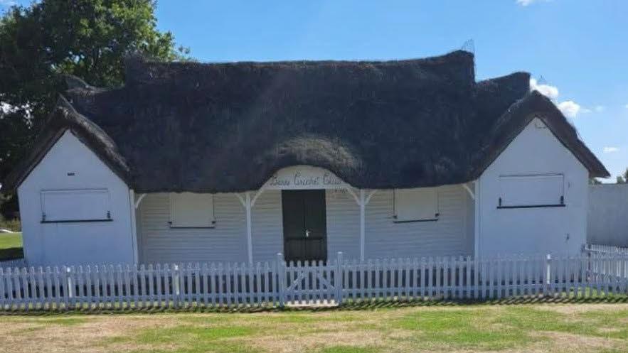 A thatched roof cricket pavilion in a grass field.