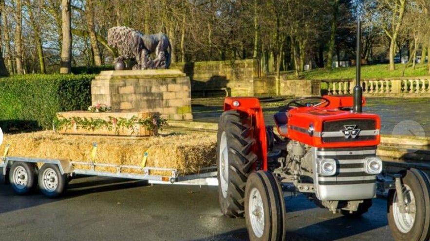 A small red Massey Ferguson 135 tractor with a trailer of hay bales attached