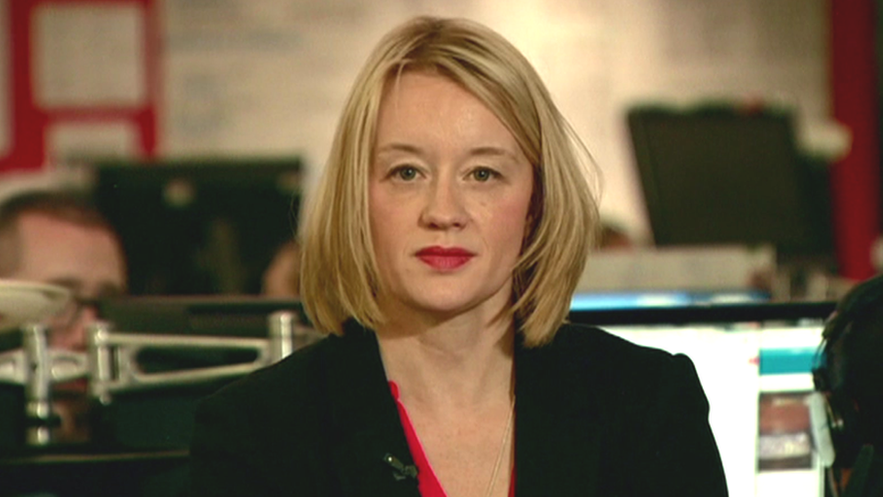 Maxine Hughes sitting in the BBC newsroom looking at the camera. She is wearing a red top and black blazer. 