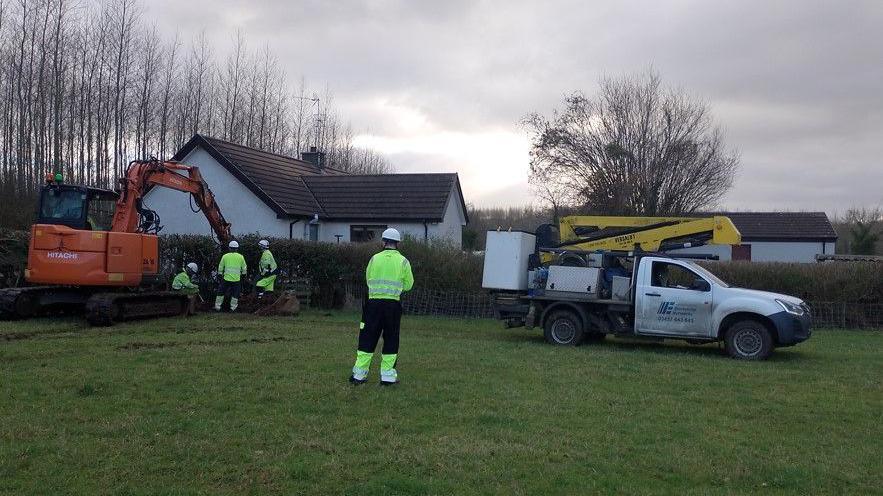 Work men in yellow high visibility clothing are working with heavy machinery at the back of a house.