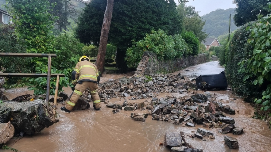 A firefighter next to a broken wall with flood water running down it