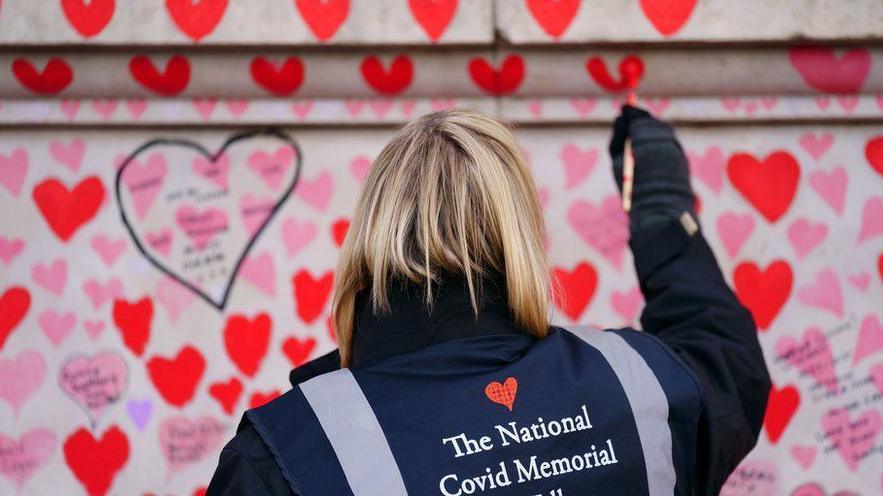 A person paints on a heart at the National Covid Memorial wall 