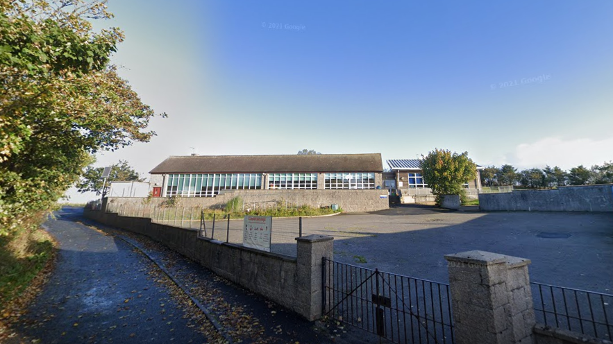 Slains School, exterior shot of rural school building and playground next to a country road and trees, under a blue sky.