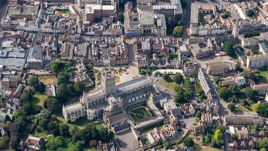 An aerial shot of Gloucester city centre on a sunny day, including Gloucester Cathedral in the foreground, green spaces, Georgian buildings, and Shire Hall