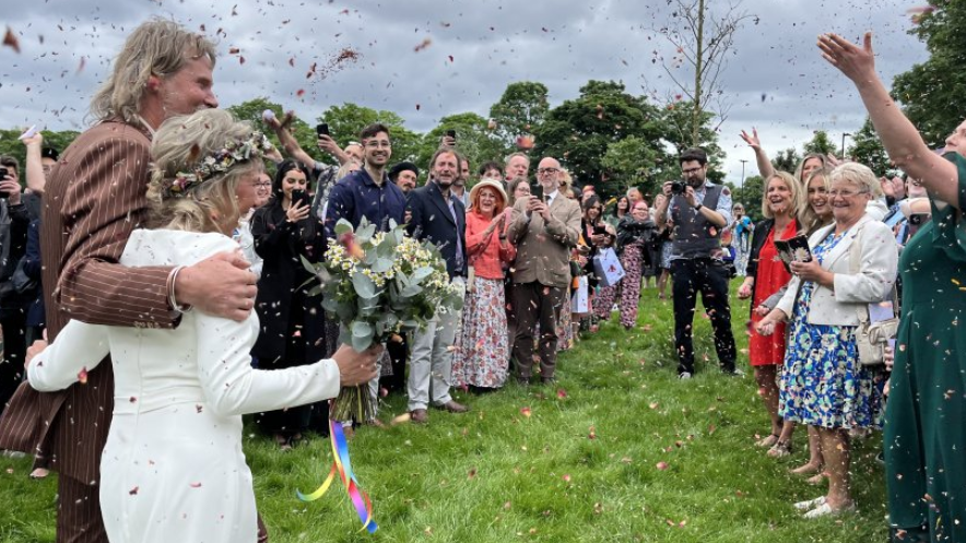 John and Sally walk through the park as guests throw confetti 