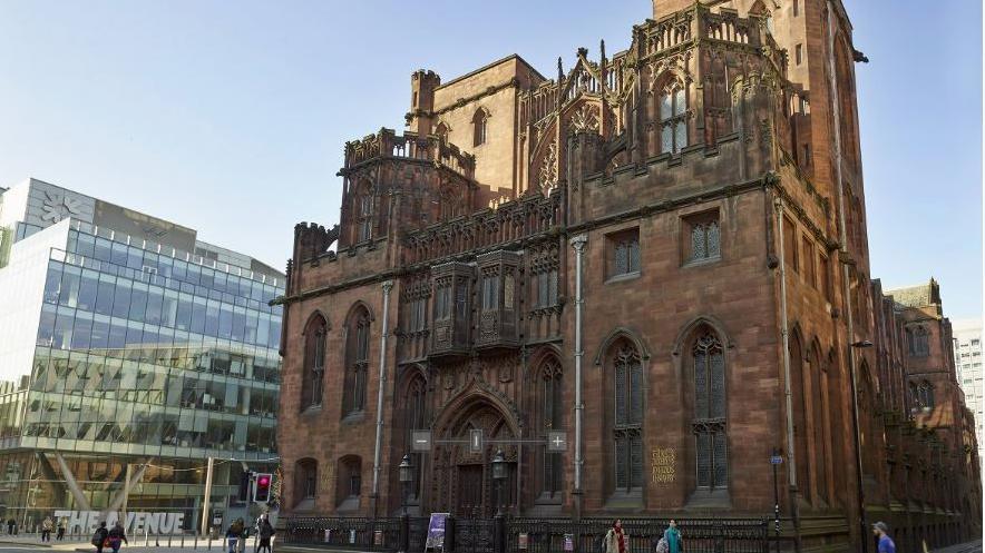 The brown neo-Gothic exterior of the multi-storied library standing imposingly on Deansgate next to a modern glass and steel building