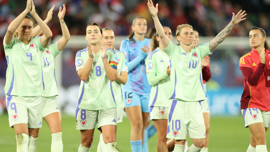 Wales players in lime green change kit applaud fans in St Gallen. Jess Fishlock is to the right with arms aloft and outstretched, Angharad James to her left applauds, and Kayleigh Barton is on the far left clapping above her head.