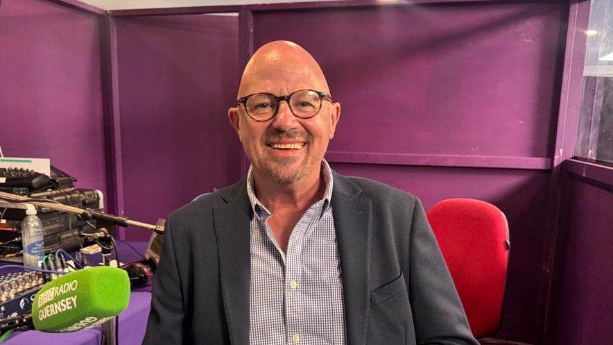 Deputy David Dorrity - A bald man with black glasses and a black jacket, with a blue and white checked shirt.