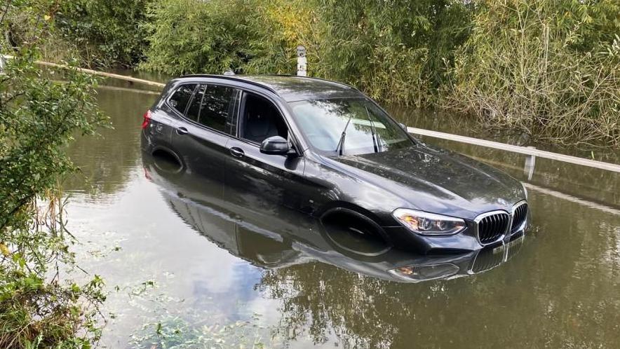 A black BMW SUV in floodwater, which is almost higher than its wheels.