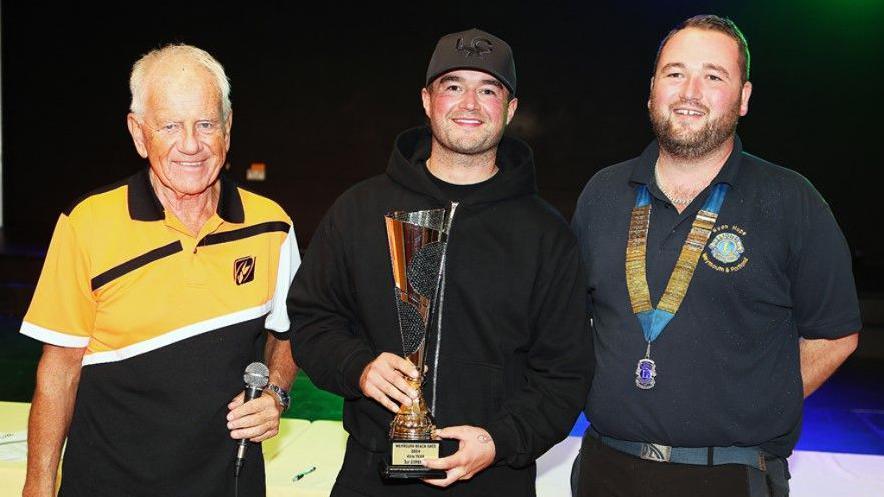 Motocross rider Jake Shipton holding his trophy and posing for the camera, standing between Ryan Hope of Weymouth and Portland Lyons Club and Mike Humphries of the Purbeck Motocross Club