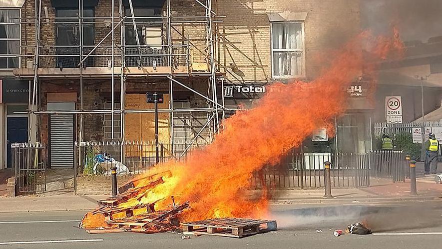 Wooden pallets on fire and burning in front of a row of terraced properties 