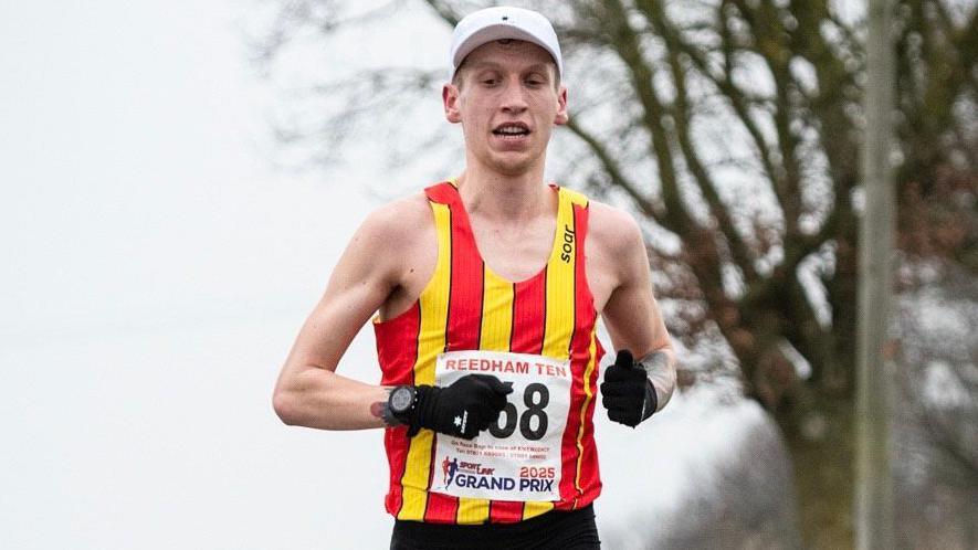 A runner is wearing a vest with vertical red and yellow stripes. 